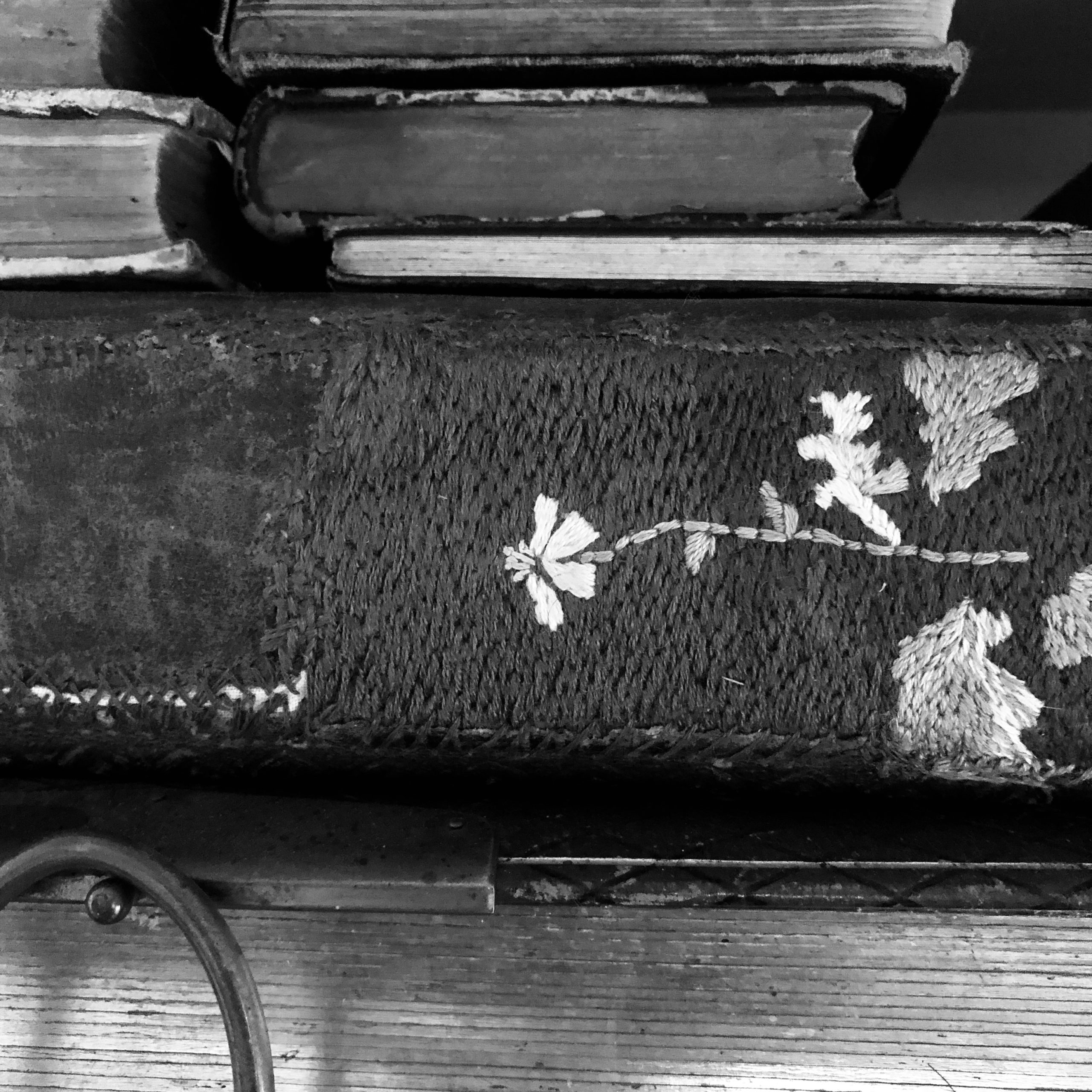 Black and white photo of stacked antique books. One has it's spine repaired with embroidery of a flower